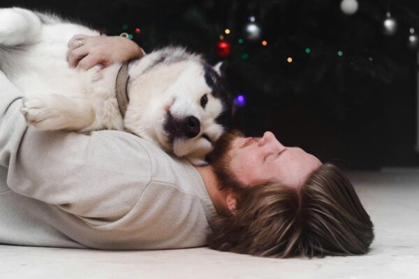 A man lying on the floor hugging a fluffy dog, showing a warm moment of connection after adoption.