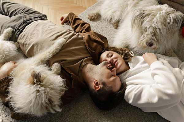 A couple lying on the floor with their dogs at home, sharing a quiet, intimate moment that reflects how everyday memories are made with pets