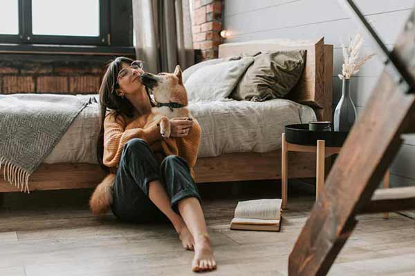Woman sitting on the floor in a cozy bedroom hugging her dog, capturing the quiet moment when a pet becomes family